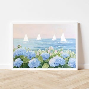 Pu&ograve; includere: Dipinto incorniciato raffigurante una scena costiera con barche a vela su un mare blu sotto un cielo rosa e blu. Il primo piano presenta vibranti fiori di ortensia blu e fogliame verde, creando un paesaggio sereno.