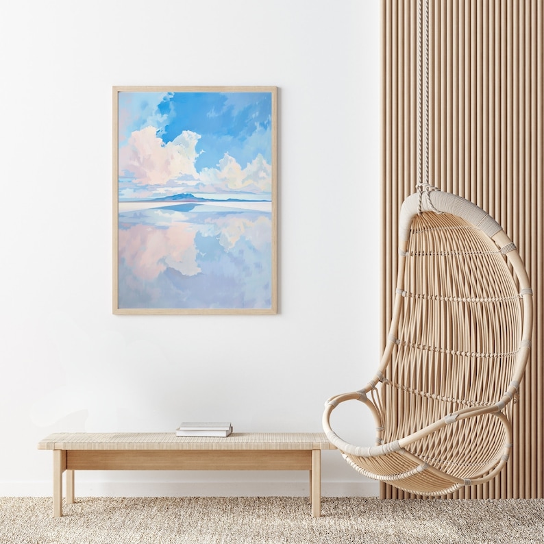 May include: A framed painting of a blue sky with white clouds reflected in a body of water. The painting is hanging on a white wall next to a light wood bench and a hanging wicker chair.