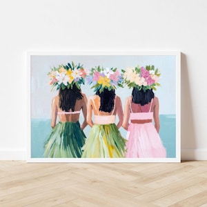 Op de afbeelding: Drie vrouwen met bloemenkransen en kleurrijke rokken staan ​​met hun rug naar de kijker. De vrouwen bevinden zich op een strand met blauw water op de achtergrond.