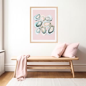 K&ouml;nnte beinhalten: Ein gerahmter Kunstdruck mit einer abstrakten Aquarellmalerei von Austern. Das Kunstwerk zeigt eine Sammlung offener Austernschalen in Blau-, Gr&uuml;n- und Cremet&ouml;nen vor einem zartrosa Hintergrund. Der Rahmen hat eine helle Holzfarbe.