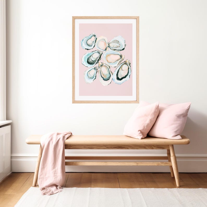 K&ouml;nnte beinhalten: Ein gerahmter Kunstdruck mit einer abstrakten Aquarellmalerei von Austern. Das Kunstwerk zeigt eine Sammlung offener Austernschalen in Blau-, Gr&uuml;n- und Cremet&ouml;nen vor einem zartrosa Hintergrund. Der Rahmen hat eine helle Holzfarbe.