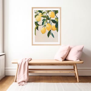 May include: A framed art print featuring a still life of lemons on a branch with green leaves. The lemons are yellow, and the leaves are green. The artwork is in a light wood frame, displayed above a wooden bench with pink pillows and a pink throw.