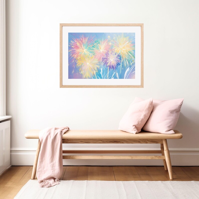 May include: A framed art print featuring a colorful fireworks display. The artwork showcases vibrant bursts of yellow, pink, blue, and purple against a light blue background. The frame is made of light-colored wood, and the print is displayed above a wooden bench.