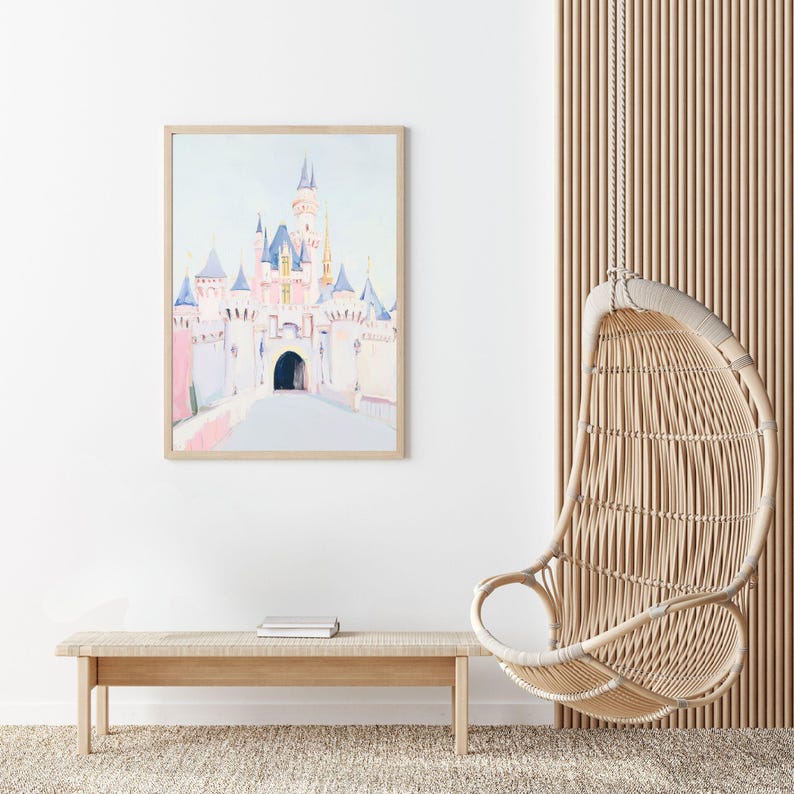 May include: A framed watercolor print of a fairytale castle in soft pink, blue, and white tones. The artwork is displayed above a light wood bench with books, next to a hanging wicker chair. The room has a neutral color palette.