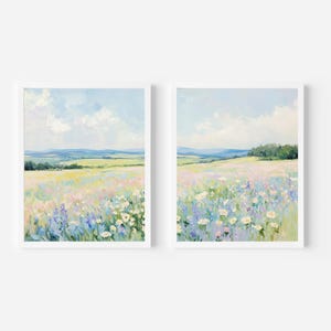 May include: Two framed landscape paintings. Each features a field of wildflowers in pastel colors, with a blue sky and distant hills. The artwork is in a soft, impressionistic style, with white frames.