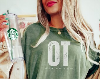 May include: A green t-shirt with the text "OT Occupational Therapist" in white. The shirt is shown in the color "moss".