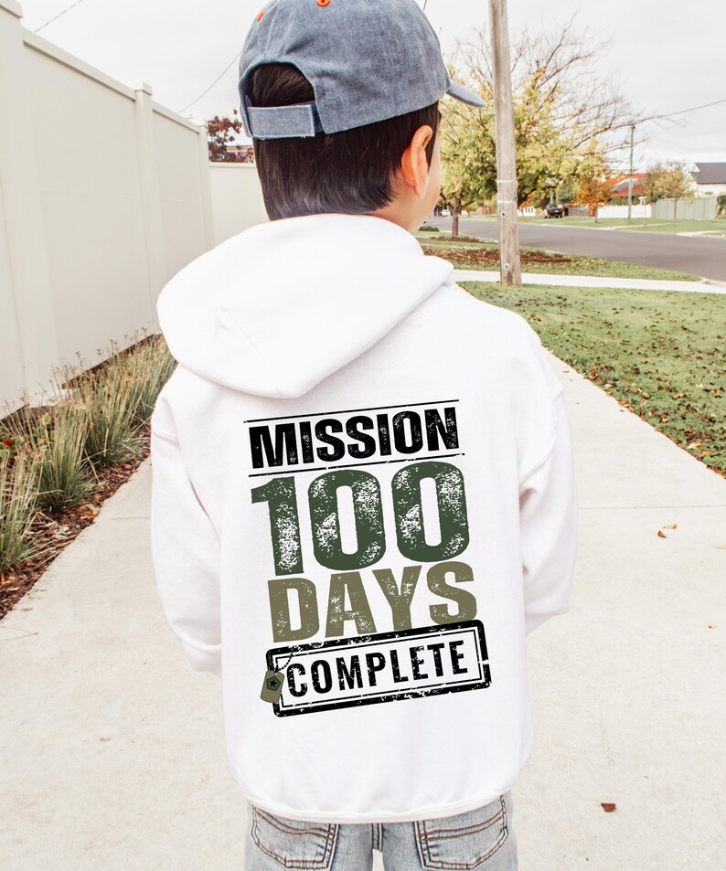 K&ouml;nnte beinhalten: Wei&szlig;er Kapuzenpullover mit dem Text "Mission 100 Days Complete" in schwarzer und gr&uuml;ner Schrift mit einem Used-Look.
