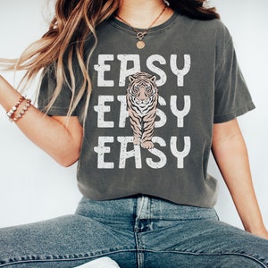 Peut inclure: Un t-shirt gris avec un motif blanc d'un tigre et le texte "EASY EASY EASY" imprim&eacute; dessus.