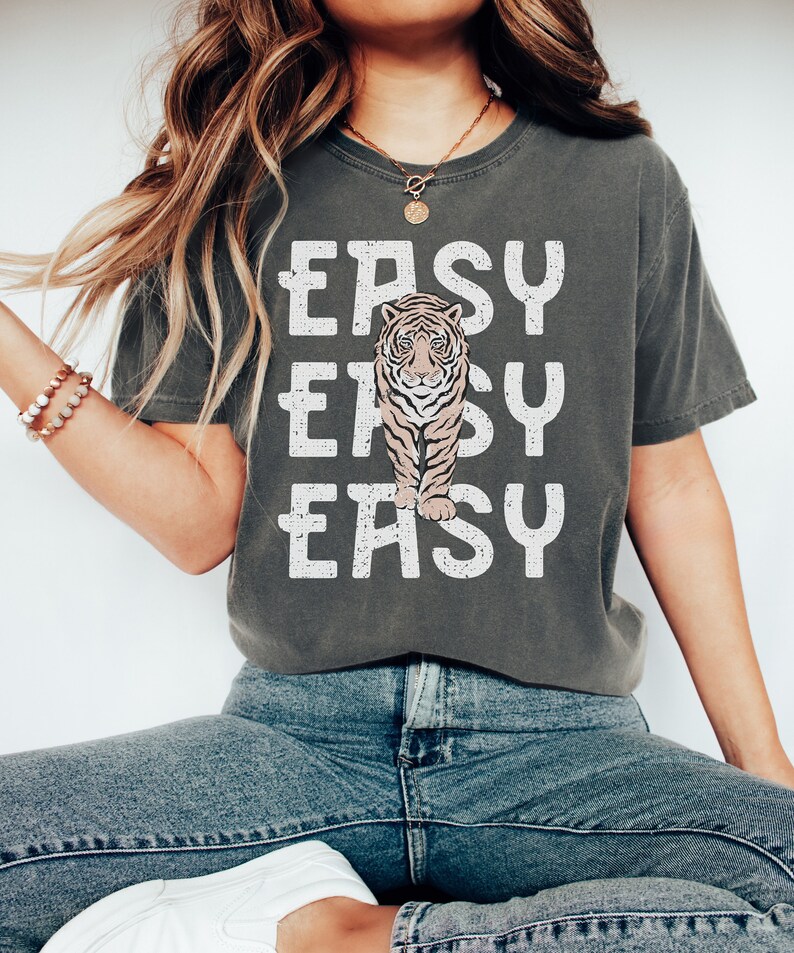 Peut inclure: Un t-shirt gris avec un motif blanc d'un tigre et le texte "EASY EASY EASY" imprim&eacute; dessus.