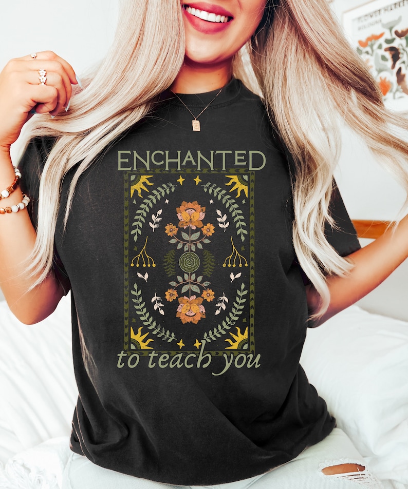 May include: A black t-shirt with a floral design and the text "ENCHANTED to teach you".