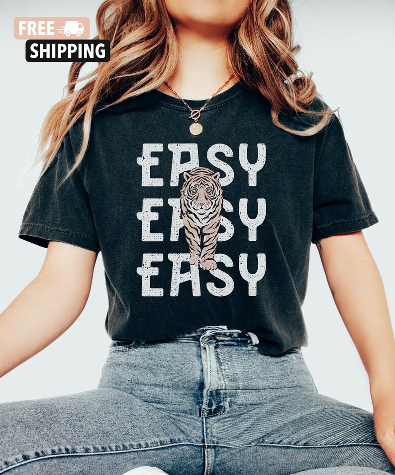 Peut inclure: Un t-shirt noir avec un motif blanc vieilli qui dit "EASY" trois fois avec une illustration de tigre au milieu.