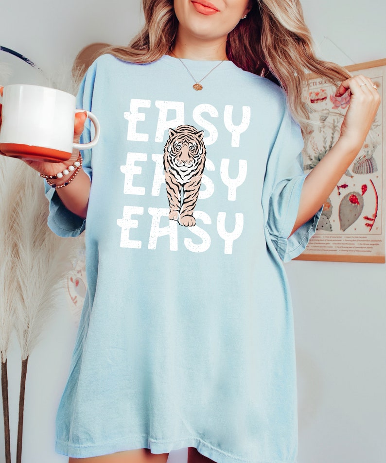 Peut inclure: Un t-shirt surdimensionn&eacute; bleu clair avec un motif blanc d'un tigre marchant avec le mot "EASY" r&eacute;p&eacute;t&eacute; trois fois.