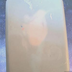 May include: A light blue bar of soap with a white swirl design. The soap has a subtle shimmer and is rectangular in shape.