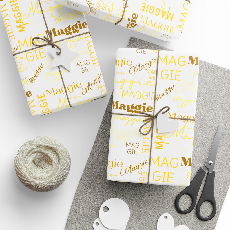 Puede incluir: Papel de regalo blanco con un patr&oacute;n repetido amarillo y marr&oacute;n del nombre "Maggie".