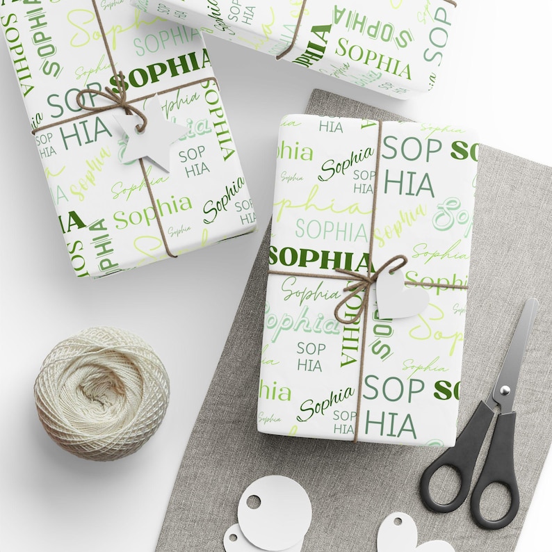Puede incluir: Papel de regalo blanco con un patr&oacute;n repetido del nombre "Sophia" en letras verdes y amarillas. El papel de regalo est&aacute; atado con cuerda y tiene una etiqueta de regalo blanca.