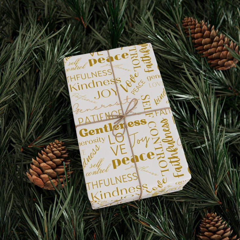 Puede incluir: Papel de regalo blanco con letras doradas. Las palabras en el papel de regalo incluyen "paz", "amor", "alegr&iacute;a", "amabilidad", "fidelidad", "paciencia", "gentileza", "autocontrol" y "generosidad".