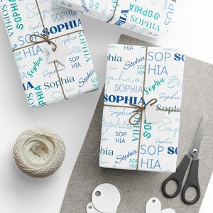 Puede incluir: Papel de regalo blanco con un patr&oacute;n azul y turquesa que presenta el nombre "Sophia" repetido en varios estilos y tama&ntilde;os.