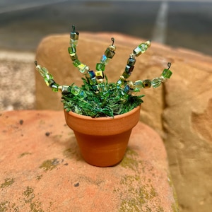 May include: A small potted plant with green moss and green iridescent glass beads arranged in a plant-like shape.