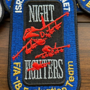 May include: A blue and black embroidered patch with the text "Israeli Hornet Night Fighters Evaluation Team" and a red and white silhouette of a fighter jet.