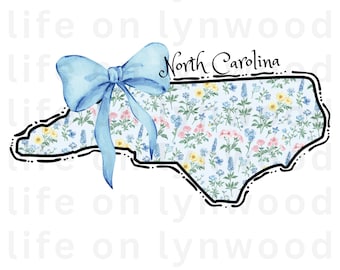May include: A blue bow sits on top of a black outline of the state of North Carolina. The state is filled with a light blue background with a floral pattern in pink, yellow, and blue.