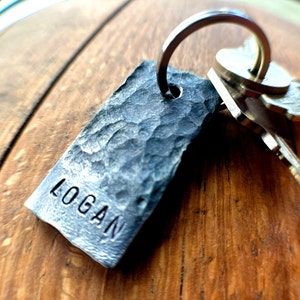 May include: A silver metal keychain with a hammered, rectangular tag that says "LOGAN".