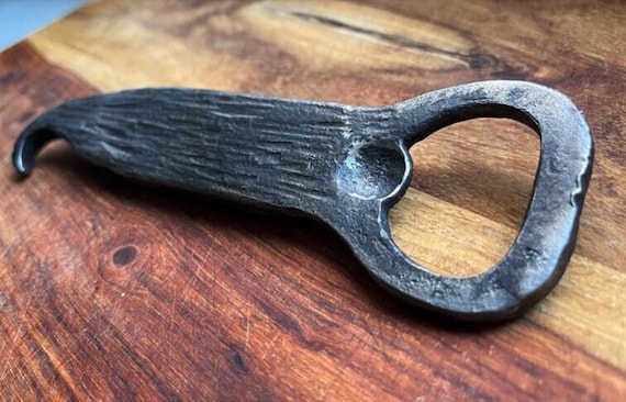 A blacksmith-forged bottle opener shaped like 'The Old Man' — a specific artistic design that signals a real craftsperson put thought into the form, not just function.