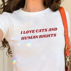 White baby tee with bold red text 'I Love Cats and Human Rights.' A feminist baby tee with a Y2K aesthetic, perfect for pro-choice messaging and gender equality advocacy.