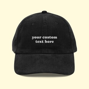 Può includere: Un cappellino da baseball in velluto a coste nero con il testo ricamato in bianco your custom text here centrato sul pannello frontale. Il cappello presenta una corona strutturata, una visiera curva e un bottone sulla parte superiore.