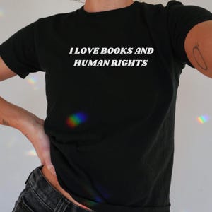 以下が含まれることがあります： 白い文字で「本と人権が好き」と書かれた黒いTシャツです。