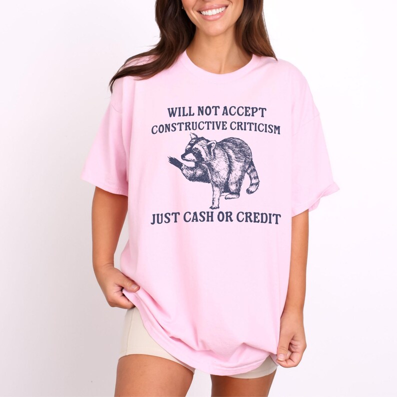 May include: Pink t-shirt with a raccoon graphic and the text "Will not accept constructive criticism, just cash or credit."