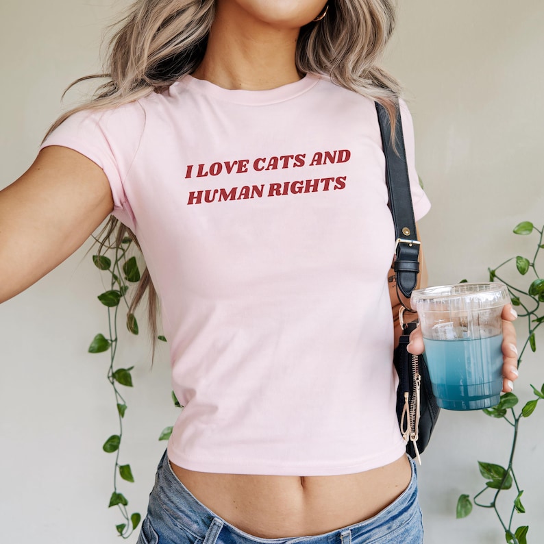 Pink baby tee featuring 'I Love Cats and Human Rights.' A cute feminist shirt blending Y2K style, social justice vibes, and an empowering women’s rights quote.