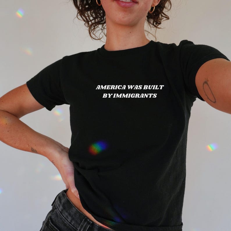Black Baby Tee With White Text "America Was Built By Immigrants". A Political Activist And Pro Immigration Shirt For Women.