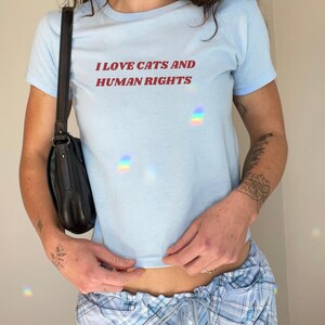 Light blue baby tee with feminism quote 'I Love Cats and Human Rights.' Feminist Y2K baby tee for cat lovers and advocates of gender equality and social justice.