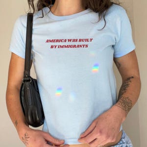 Y2k Baby Tee In Blue With Red Text "America Was Built By Immigrants". A Political Activist And Pro Immigration Tee For Women.