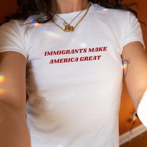May include: White t-shirt with the text "Immigrants Make America Great" printed in red.