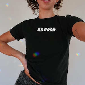 May include: Black crew neck t-shirt with the white text "BE GOOD" across the chest. The shirt is a solid black color and appears to be made of a soft material. The shirt is a casual style.