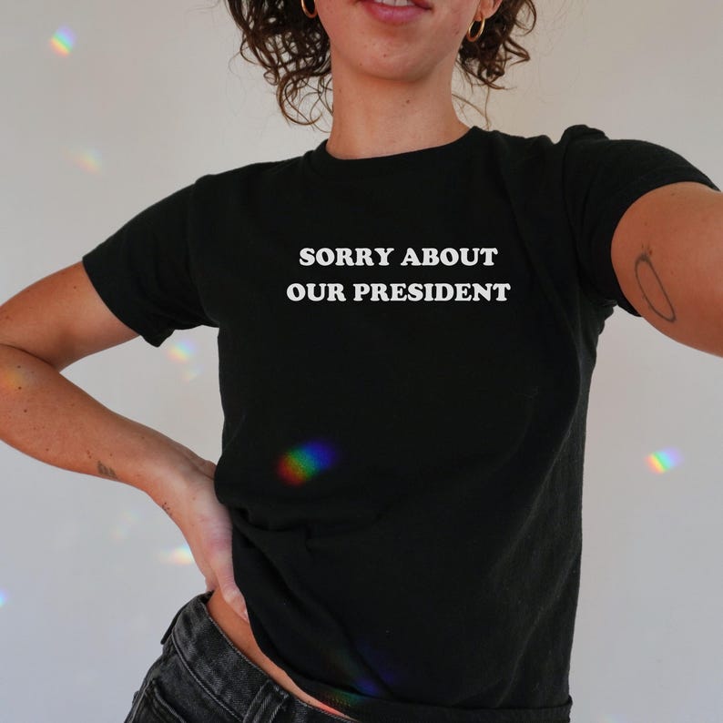 Black Y2K baby tee with white text that reads 'Sorry About Our President.' Anti-MAGA shirt, feminist baby tee, progressive liberal shirt for women.