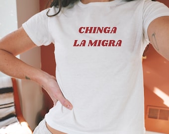 May include: White t-shirt with the text "CHINGA LA MIGRA" printed in red.