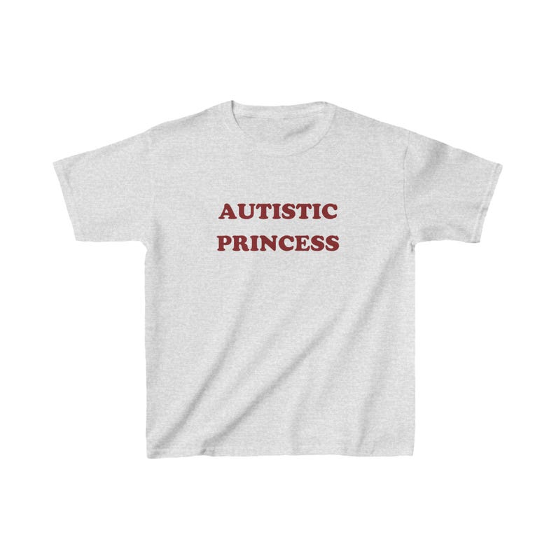 以下が含まれることがあります： 薄いグレーのTシャツに「AUTISTIC PRINCESS」という文字がマルーンでプリントされています。