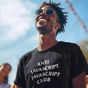 May include: A man wearing sunglasses and a black t-shirt with the text "ANTI JAVASCRIPT JAVASCRIPT CLUB" printed in white. He is smiling and looking up at the sky.