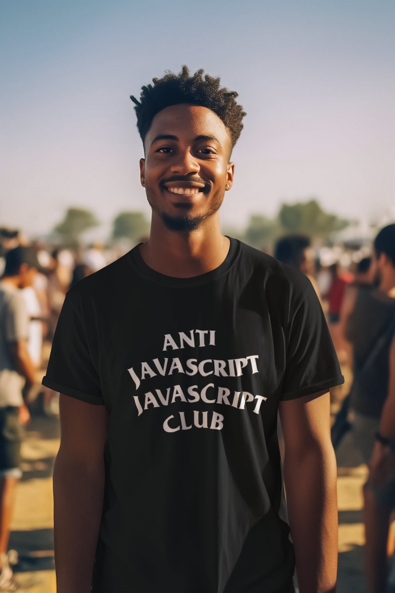May include: A man wearing a black t-shirt with white text that reads "ANTI JAVASCRIPT JAVASCRIPT CLUB". He is smiling and standing in front of a crowd of people.