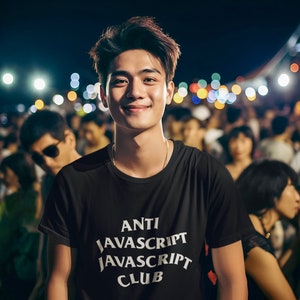 May include: A man wearing a black t-shirt with the text "ANTI JAVASCRIPT JAVASCRIPT CLUB" in white. He is standing in a crowd of people at a concert or event.