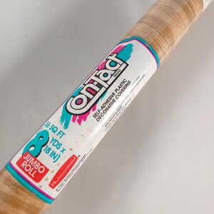 May include: A jumbo roll of Contact brand self-adhesive plastic decorative covering with a light brown wood grain pattern. The label features the text Contact, Self-Adhesive Plastic Decorative Covering, 36 SQ FT, 8 YDS x 18 IN, and Rubbermaid.