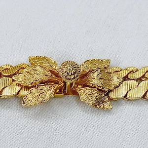 May include: Gold tone chain bracelet with a leaf and flower design clasp.