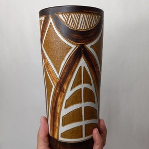 May include: A brown ceramic vase with a geometric pattern in white and brown. The vase has a cylindrical shape and a wide mouth.