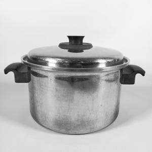 Könnte beinhalten: Ein Kochtopf aus Edelstahl mit Deckel und zwei schwarzen Griffen. Der Topf hat eine glänzende, reflektierende Oberfläche und einen schwarzen Knopf auf dem Deckel. Der Topf ist zum Kochen und zur Zubereitung von Speisen bestimmt.