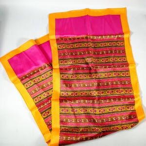 May include: Two silk scarves in a vibrant colour scheme. The scarves feature a bright pink centre with a patterned design in gold, red, and brown. The edges are bordered with a bright yellow.