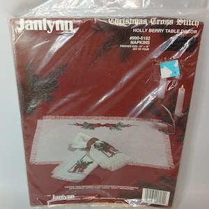 May include: A Janlynn Christmas cross stitch kit, featuring a holly berry table decor design. The kit includes napkins with a finished size of 45.72 cm x 45.72 cm. The package is sealed in clear plastic.