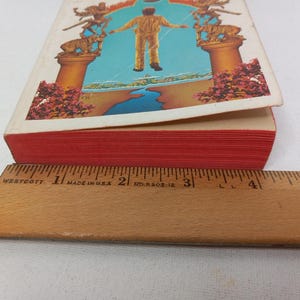 Puede incluir: Un libro de tapa dura rojo con una ilustraci&oacute;n colorida en la portada. La ilustraci&oacute;n representa a una persona de pie en una puerta con un cielo azul y agua en el fondo.