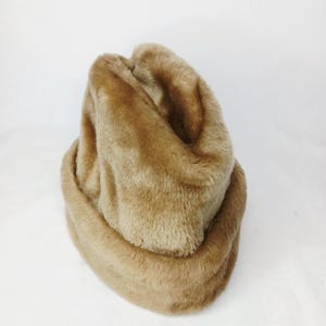 Könnte beinhalten: Ein beigefarbener Kunstfellhut. Der Hut besteht aus einem weichen, plüschigen Material mit einer abgerundeten Form. Der Hut hat eine neutrale Farbe und wirkt warm und gemütlich. Der Hut ist wahrscheinlich für kaltes Wetter.